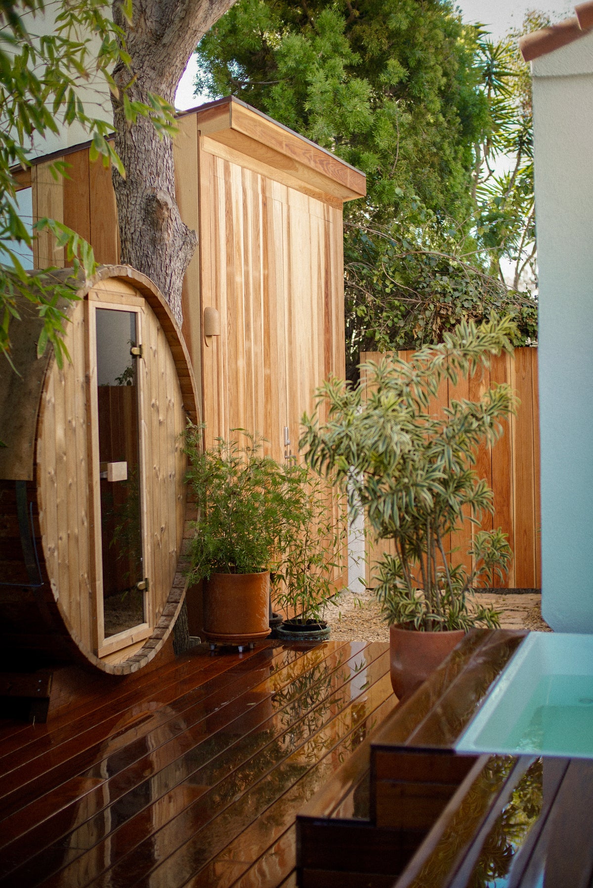 Barrel sauna beside a cold plunge pool on a wet courtyard deck.