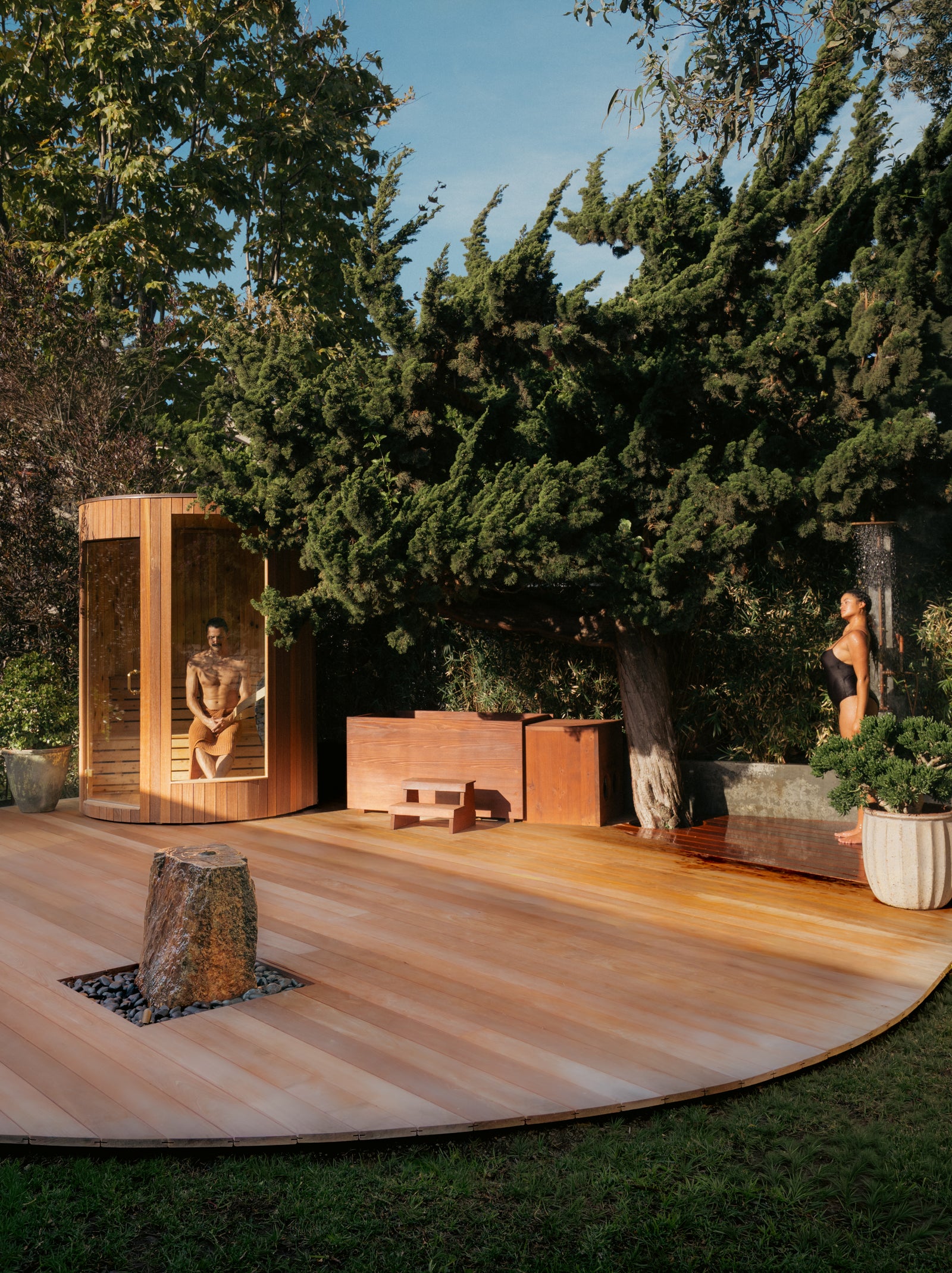Cedar bathing deck at golden hour with sauna and soaking tub under old trees.